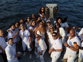 A vibrant group of friends celebrates together on a boat, all dressed in white, capturing the joy of a memorable outing on the water.