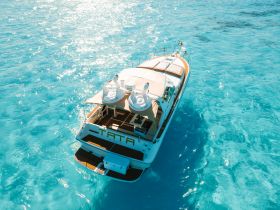 A stunning aerial view of a luxurious yacht cruising through crystal-clear turquoise waters, showcasing its elegant design and vibrant surroundings.