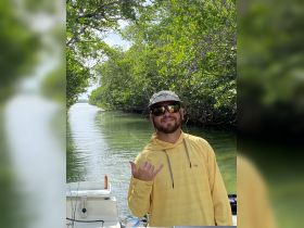 A smiling individual gives a shaka sign while enjoying a fishing trip through scenic mangroves — a perfect moment for adventure seekers.