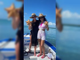 Two friends pose with starfish while enjoying a sunny day on the water in Belize — a memorable wildlife encounter perfect for marine enthusiasts.