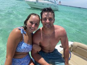 A cheerful couple enjoys a sunny day on the water, capturing a fun moment while relaxing on their boat in crystal-clear waters.