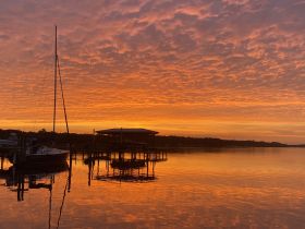 A serene sunset view featuring a sailboat docked by the water, reflecting vibrant orange hues — perfect for capturing the tranquility of evening on the water.