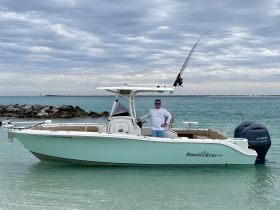 A man stands proudly next to his NauticStar boat in clear waters, ready for a day of fishing. The scenic backdrop highlights the beauty of ocean adventures.