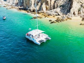An aerial view of a lively catamaran anchored near a stunning coastline, showcasing the perfect blend of adventure and relaxation in a picturesque setting.