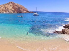 A vibrant scene of snorkelers enjoying the clear waters near a rocky coastline, with boats anchored nearby — a perfect destination for water activities and beach fun.