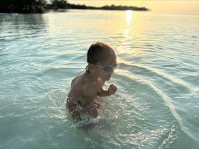 A joyful child splashes in the shallow waters during sunset, capturing the essence of fun and adventure in a tropical paradise.