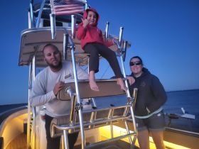 A family enjoys a fun moment aboard a boat at dusk, with a child playfully posing on the ladder — perfect for capturing joyful boating experiences.