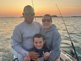 A family enjoys a beautiful sunset while fishing on a boat, capturing a memorable moment together on the water.