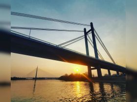 A stunning sunset view framed by a bridge, reflecting beautifully on the water — a perfect moment for capturing the serene beauty of nature.