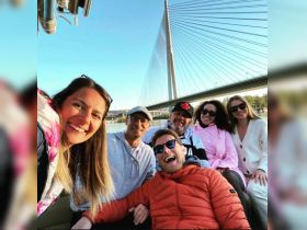 A joyful group of friends poses for a selfie on a boat, with a stunning bridge in the background — perfect for capturing memorable moments on the water.
