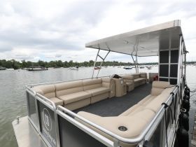 Interior view of a spacious lounge area on a pontoon boat, featuring comfortable seating and a shaded canopy, perfect for relaxing on the water.