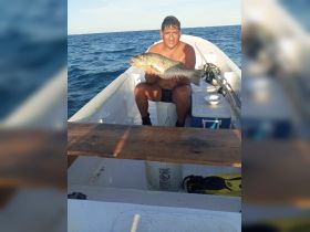 A proud angler displays his impressive catch aboard a small fishing boat, showcasing the thrill of a successful day on the water.