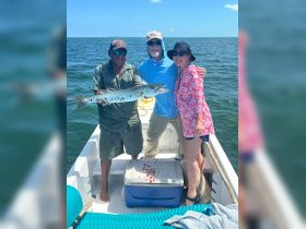 A group celebrates a successful fishing trip, proudly displaying their catch of a barracuda aboard a boat — a perfect moment for fishing enthusiasts.