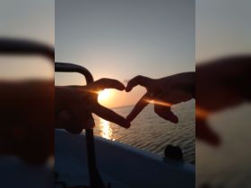 A romantic moment captured as two hands form a heart shape against a stunning sunset backdrop on the water, perfect for couples celebrating love.