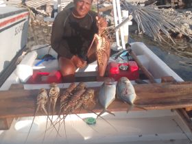 A fisherman proudly displays his catch of lobsters and fish on a small boat, showcasing the bounty of the sea — perfect for seafood lovers and fishing enthusiasts.
