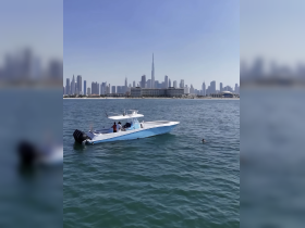 A boat is anchored in the vibrant waters of Dubai, with a swimmer nearby and the iconic skyline in the background, showcasing a perfect day on the water.