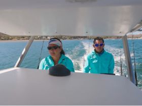 Two individuals navigate a boat, showcasing the experience of being on the water. Ideal for highlighting boating adventures and crew interactions.