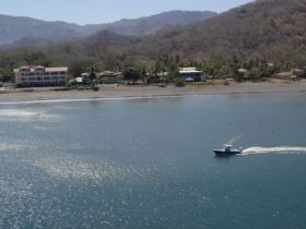 An aerial view of a speedboat cruising through calm waters, with a picturesque beach and lush greenery in the background, perfect for showcasing coastal adventures.