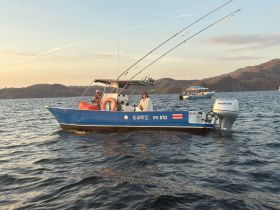 Two people enjoy a fishing trip aboard a blue boat during sunset, surrounded by scenic ocean views — a perfect moment for adventure on the water.