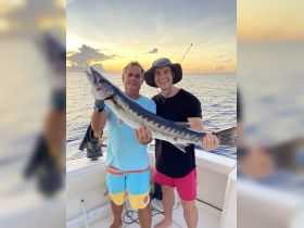 Two anglers proudly display their catch against a stunning sunset backdrop while fishing on the water — a perfect moment of celebration on a fishing trip.