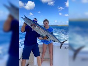A successful fishing trip captures a young girl and an adult proudly displaying a large wahoo catch, showcasing the thrill of deep-sea fishing.