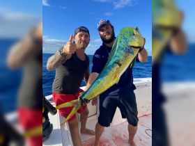 Two anglers proudly display their impressive catch while fishing in the ocean, showcasing the thrill of a successful day on the water.