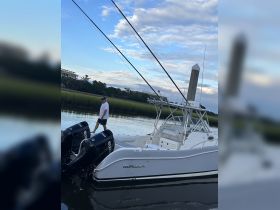 A man walks along the deck of a World Cat boat, surrounded by tranquil waters and lush greenery — a perfect scene for fishing enthusiasts.