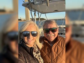 A cheerful couple poses for a selfie on a boat, enjoying a beautiful sunset — perfect for romantic outings or memorable adventures on the water.