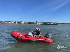 A couple enjoys a scenic ride on a red inflatable boat, surrounded by beautiful waterfront views — perfect for a day of adventure on the water.