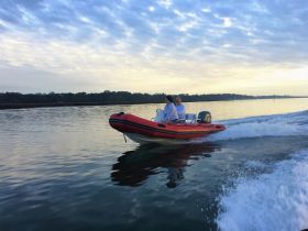 A couple enjoys a thrilling ride on a speedboat, gliding across calm waters under a beautiful sky — perfect for adventure seekers and romantic outings.