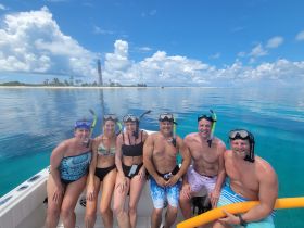 A cheerful group of snorkelers poses for a photo on their boat, with a picturesque lighthouse and serene waters in the background — a perfect snapshot of their aquatic adventure.