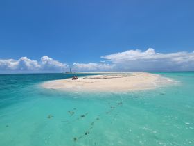 A couple relaxes on a picturesque sandbar surrounded by crystal-clear waters, perfect for a romantic getaway or island hopping adventure.