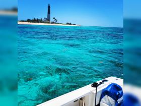 A stunning view of a lighthouse along a picturesque coastline, with vibrant turquoise waters in the foreground — an ideal setting for a relaxing day on the water.