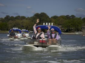 A lively group enjoys a fun day on the water, waving from their boat as they cruise through scenic waterways — perfect for memorable outings with friends.