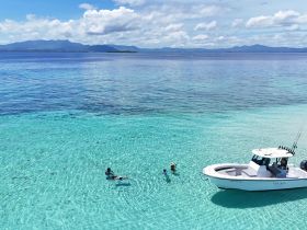 A family enjoys a refreshing swim in the crystal-clear turquoise waters, with a boat anchored nearby, creating the perfect backdrop for a fun day on the water.