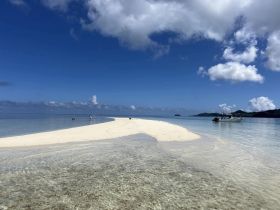 A picturesque sandbar with guests enjoying the serene beach and clear waters, while a boat is anchored nearby — an ideal spot for relaxation and exploration.