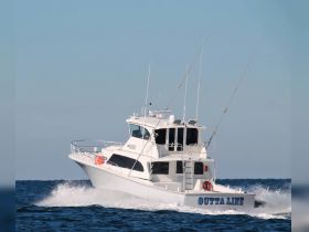 A sleek fishing boat named 'OUTTA LINE' speeds through the open water, showcasing its impressive design and performance.