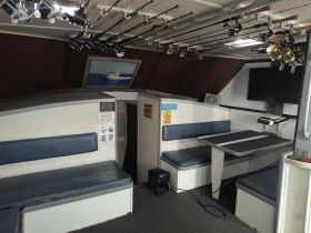 Interior view of a fishing boat cabin featuring seating, fishing rods, and a TV, ideal for comfortable outings on the water.