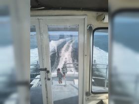 A view from the helm of a boat showing a crew member navigating the waters, capturing the essence of boating adventures and the operational side of maritime experiences.