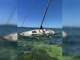 A partially submerged sailboat in clear waters, showcasing the hull and rigging — a striking image of a marine wreck.