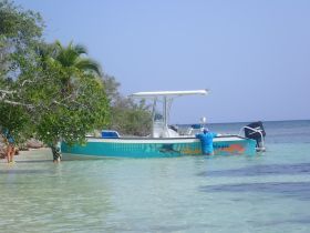 A boat is anchored in shallow waters near a beach, with individuals enjoying the serene environment — a perfect setting for a day of adventure and relaxation.