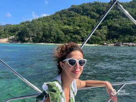 A woman enjoys a sunny day on a boat, with a stunning beach and lush greenery in the background — perfect for tropical adventures and relaxation on the water.