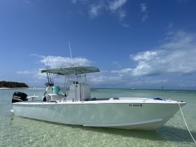 A sleek speedboat anchored in shallow turquoise waters, showcasing its pristine design against a backdrop of clear skies and distant islands — perfect for fishing or leisure outings.