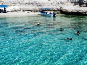 A group enjoys a refreshing swim in crystal-clear waters, with a boat anchored nearby — perfect for a day of snorkeling and fun in the sun.
