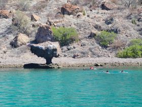 A group of swimmers enjoys the clear waters near a unique rock formation, showcasing the stunning natural scenery perfect for outdoor adventures.