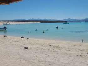 A vibrant beach scene with people enjoying swimming and snorkeling in crystal-clear waters, perfect for a fun day under the sun.
