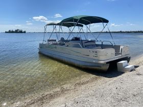 A pontoon boat named 'Summit' is docked on a sandy shore, surrounded by calm waters and a clear blue sky, perfect for leisurely outings.