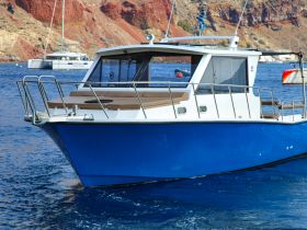 A striking view of a blue boat anchored in clear waters, showcasing its sleek design against a backdrop of rocky cliffs.
