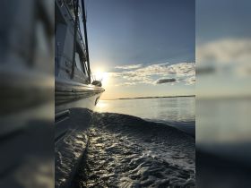 A stunning side view of a yacht cruising through calm waters at sunset, showcasing the vessel's sleek design against a picturesque sky.