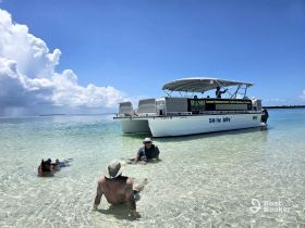 A group enjoys a relaxing day at a sandbar, wading in crystal-clear waters near the pontoon boat 'SNOW DAY' — perfect for summer fun and aquatic adventures.